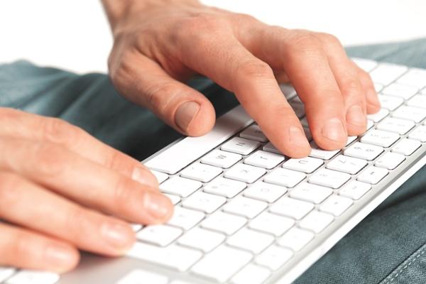Zwei Hände ruhen auf einer auf dem Schoß liegenden Tastatur.