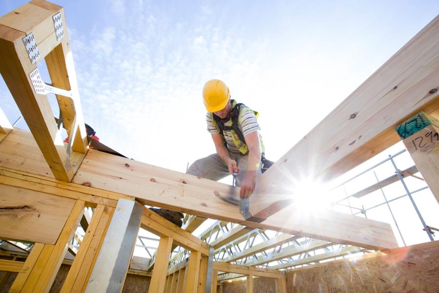 Ein Handwerker mit gelbem Helm baut an dem Dachstuhl eines neu gebauten Hauses.