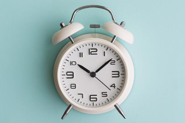 Ein weißer Wecker vor blauem Hintergrund zeigt die Uhrzeit 10:08 Uhr.